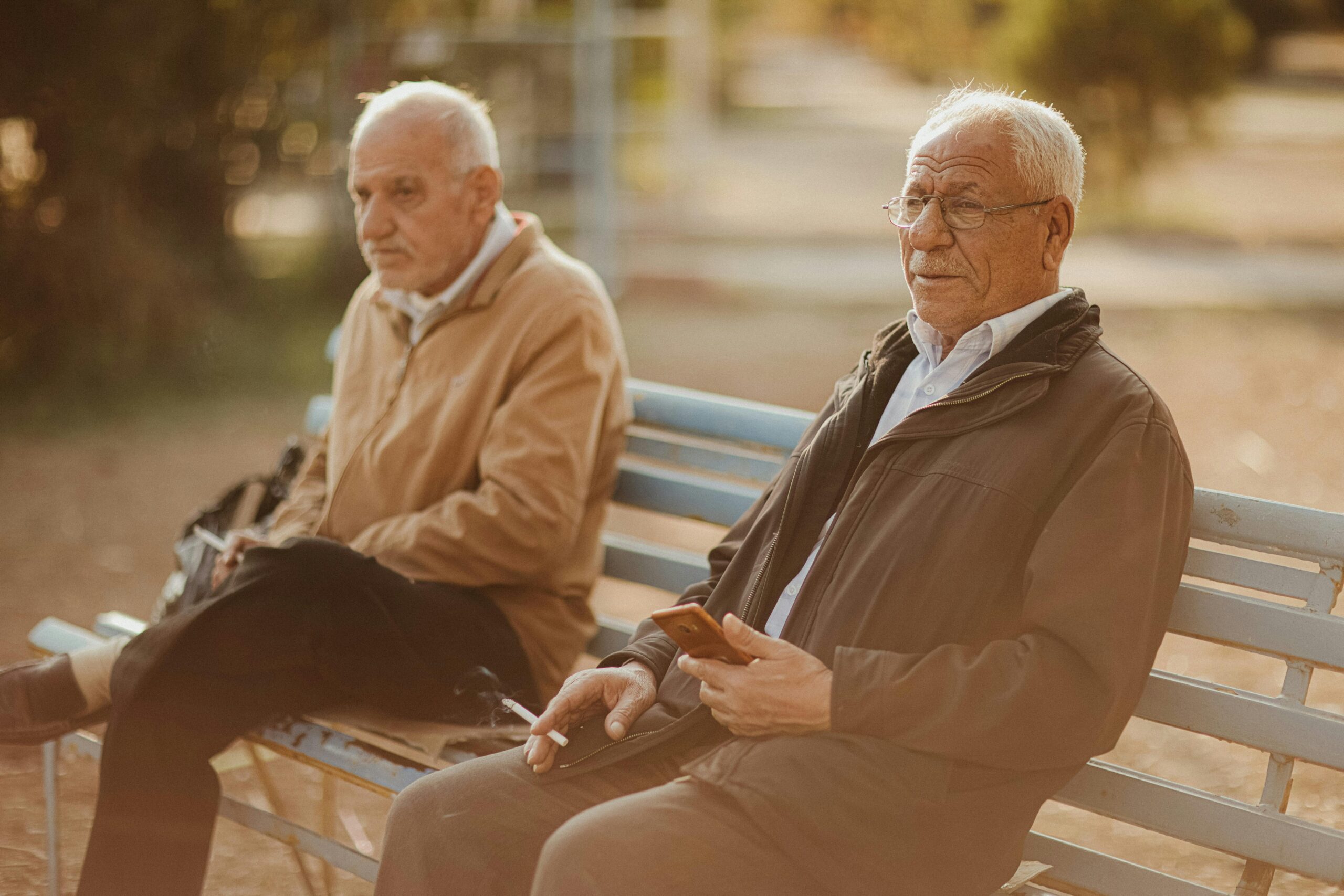Two senior men sitting on a bench outdoors, enjoying a casual moment.